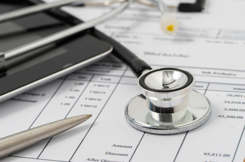 A stethoscope, calculator, and pen lay on top of medical billing documents.