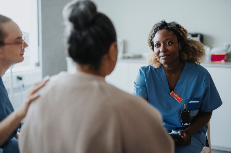 A female medical provider talks to a patient and her caregiver in a clinical setting.